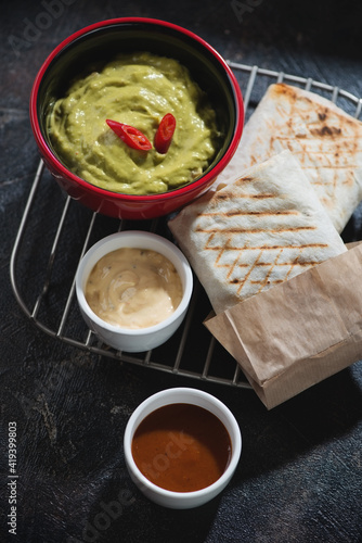 Shawarma with meat and vegetable filling and dips on a metal cooling rack, studio shot on a dark brown stone surface