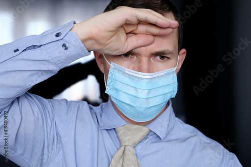 Coronavirus and fever symptoms, man in face mask and office clothes put his hand on forehead. Sick office worker, concept of headache, pressure or cold and flu