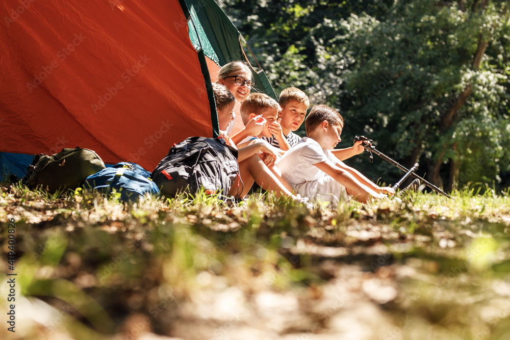 Group of school children sitting in tent with they female teacher. - obrazy, fototapety, plakaty 