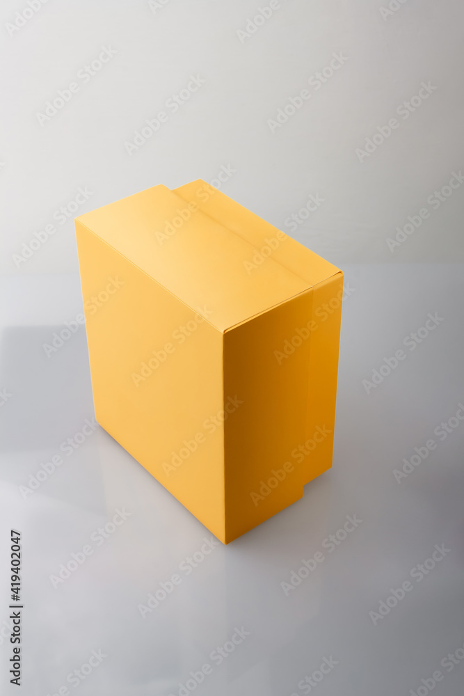 Fototapeta premium Yellow orange closed cardboard box or carton on grey background, template, mockup, sideview.