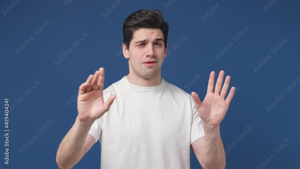 Confused young man 20s years old in casual white t-shirt posing isolated on blue color background in studio. People lifestyle concept. Pointing finger himself ask say who me no thanks i do not need it Confused young man 20s years old in casual white t-shirt posing isolated on blue color background in studio. People lifestyle concept. Pointing finger himself ask say who me no thanks i do not need it