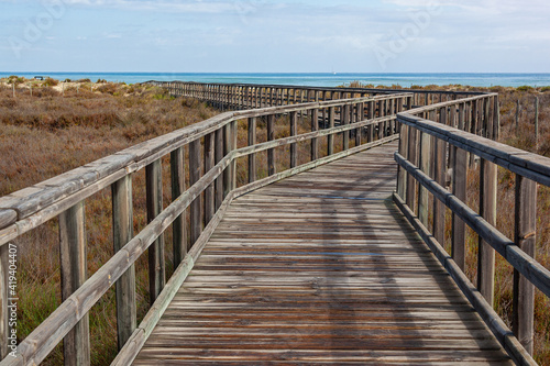 Fototapeta Naklejka Na Ścianę i Meble -  A wooden boardwalk leading through coastal marshlands and sand dunes to the sea beach at San Pedro del Pinatar park, Murcia, Spain