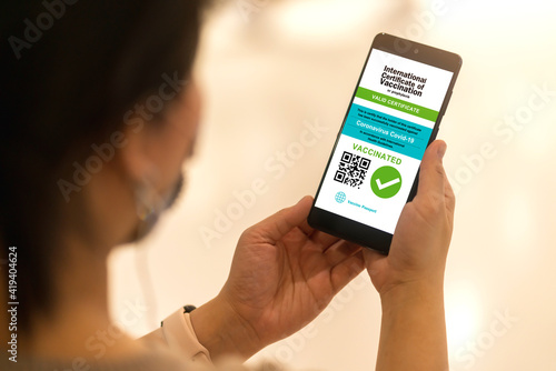 Smartphone displaying a valid digital vaccination certificate passport for COVID-19 in female's hand, public area background. Vaccination, disease immunity passport, health and safty travel concepts