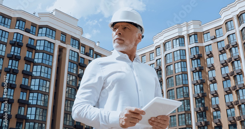 Low angle view of mature engineer using digital tablet with building on urban street at background