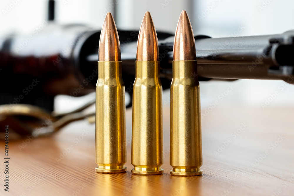 Three bullets against blurred Kalashnikov assault rifle background. Cartridges 7.62 caliber for ak 47 closeup Three bullets against blurred Kalashnikov assault rifle background. Cartridges 7.62 caliber for ak 47 closeup