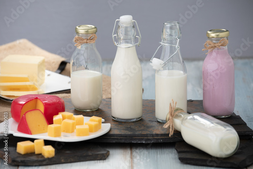 Bottles of milk and yogurt on a wooden table with cheese plater on a grey background