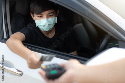 A young man wearing protective mask used credit card for payment at drive thru food service. Outbreak COVID-19, Medical, Healthcare and Quarantine concept.