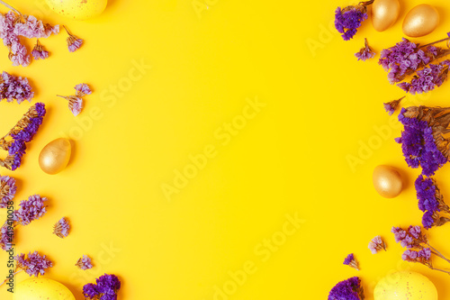 Easter yellow eggs with purple flowers on yellow background. Flat lay, copy space.