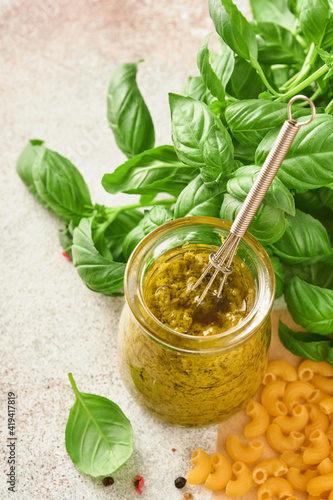 Jar with homemade pesto sauce on rustic background with parmesan cheese, olive oil, sause pesto, basil and garlic. Copy space background.
