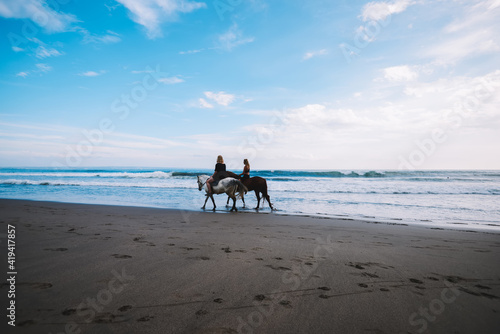 Unrecognizable female tourists riding horses along coastline