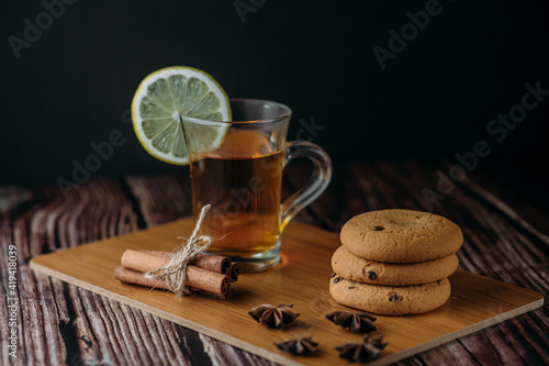 A cup of hot fruit tea or mulled wine on a wooden board. Nearby are biscuits, cinnamon and star anise. Copy space