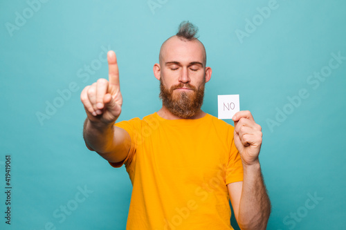 Bearded european man in yellow shirt isolated on turquoise background holding no strong man serious face