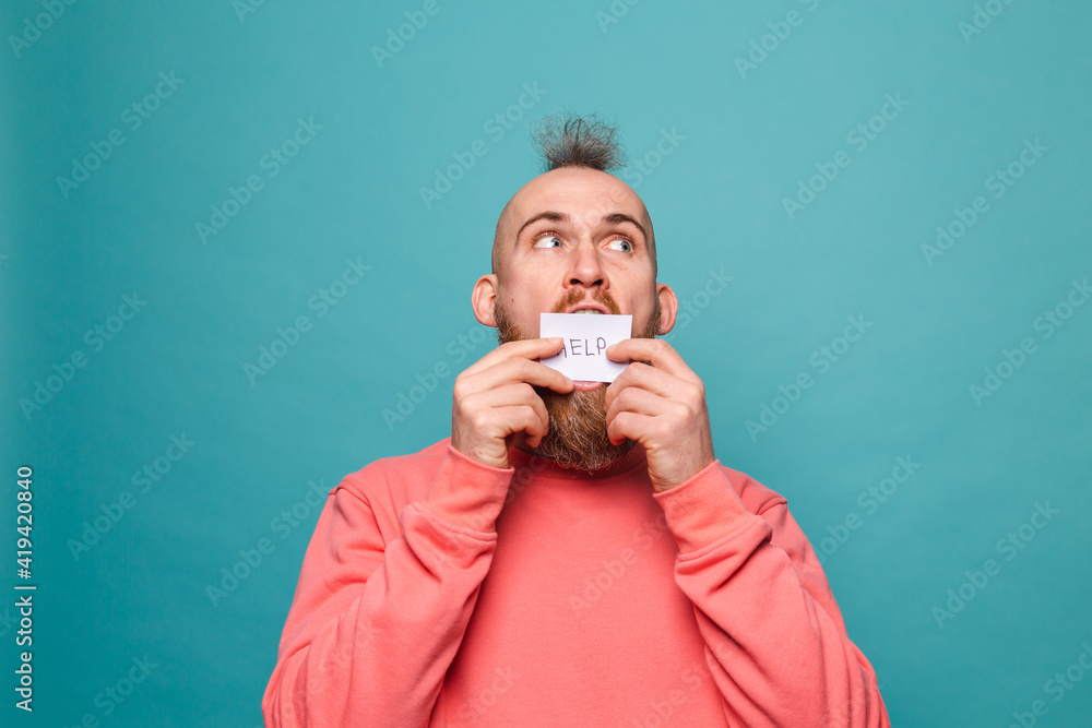 Bearded european man in casual peach isolated on turquoise background holding paper with help sign brutal with serious face Bearded european man in casual peach isolated on turquoise background holding paper with help sign brutal with serious face