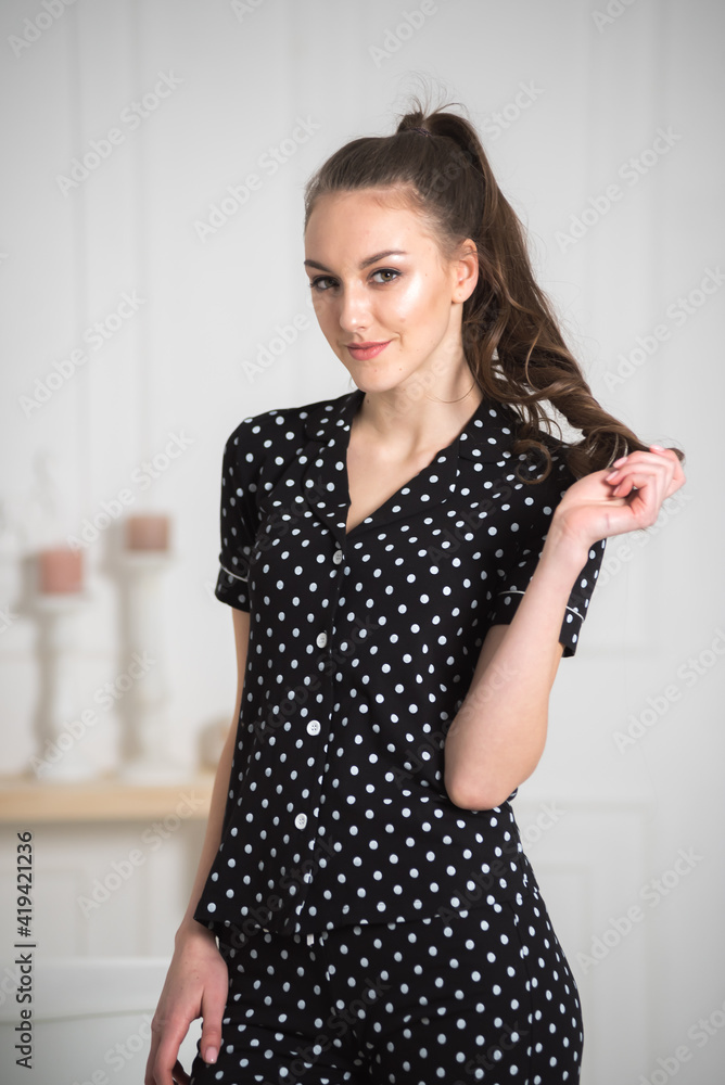 Young attractive woman dressed in beautiful pajama posing as a model in her living room. Comfortable sleepwear, home relaxation and female fashion concept.
