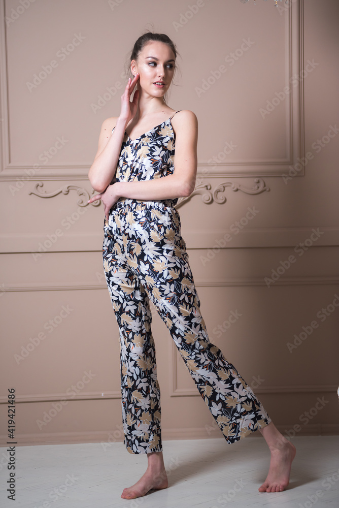 Young attractive woman dressed in beautiful pajama posing as a model in her living room. Comfortable sleepwear, home relaxation and female fashion concept. Young attractive woman dressed in beautiful pajama posing as a model in her living room. Comfortable sleepwear, home relaxation and female fashion concept.