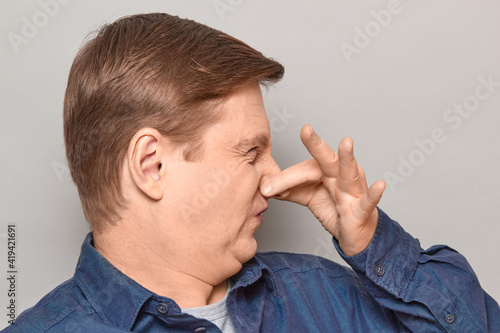 Portrait of mature man pinching his nose and grimacing from disgust photo