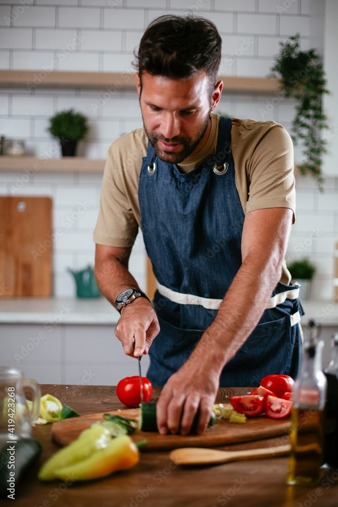 Young man preparing vegetable salad in the kitchen. Happy man making healthy meal. Young man preparing vegetable salad in the kitchen. Happy man making healthy meal.