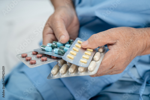 Asian senior or elderly old lady woman patient holding antibiotics capsule pills in blister packaging for treatment infection patient in hospital : Pharmacy drugstore concept.