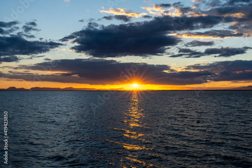 scenic and colorful sunset over the ocean with shimmering light on the waves and silhouette of mountains on the shore behind