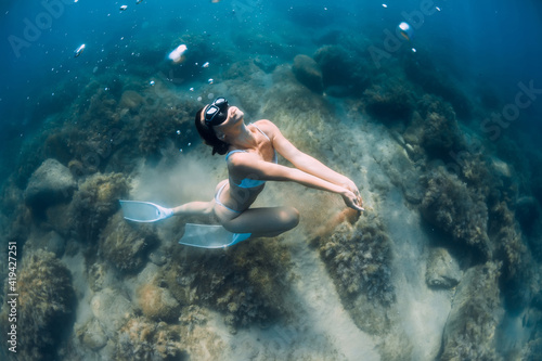 Woman glides with sand in hand. Free diver with fins posing underwater