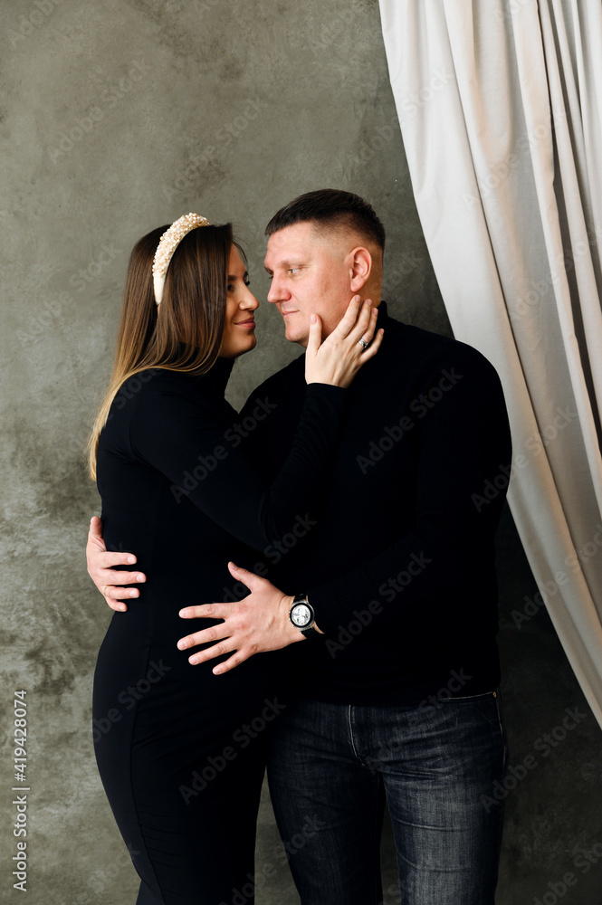 beautiful pregnant couple dressed in beautiful black clothes hugs. pregnant woman in a dress hugs her husband at home. a pregnant family rejoices in the future replenishment