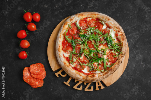 Homemade Pepperoni pizza with Mozzarella cheese, salami, tomato sauce, pepper, arugula and spices. Italian pizza on a dark gray black background