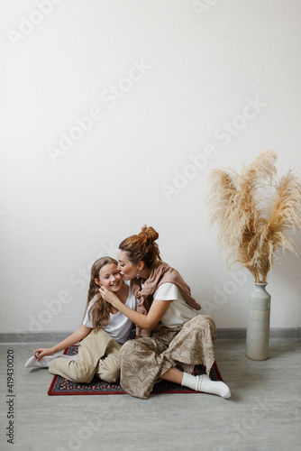 Mom kisses her laughing daughter on the cheek while sitting on the floor