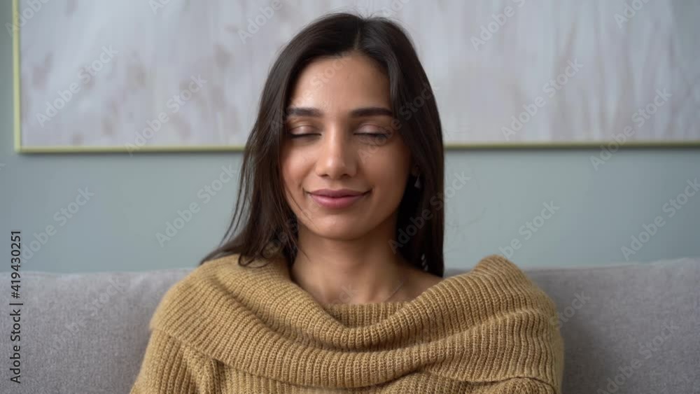 Attractive Indian mixed-race woman looking at camera sit on sofa alone at home Attractive Indian mixed-race woman looking at camera sit on sofa alone at home