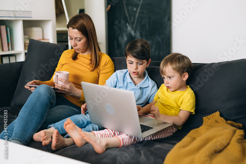 asocial family. mother and two sons sitting on sofa and using laptop computer and digital tablet