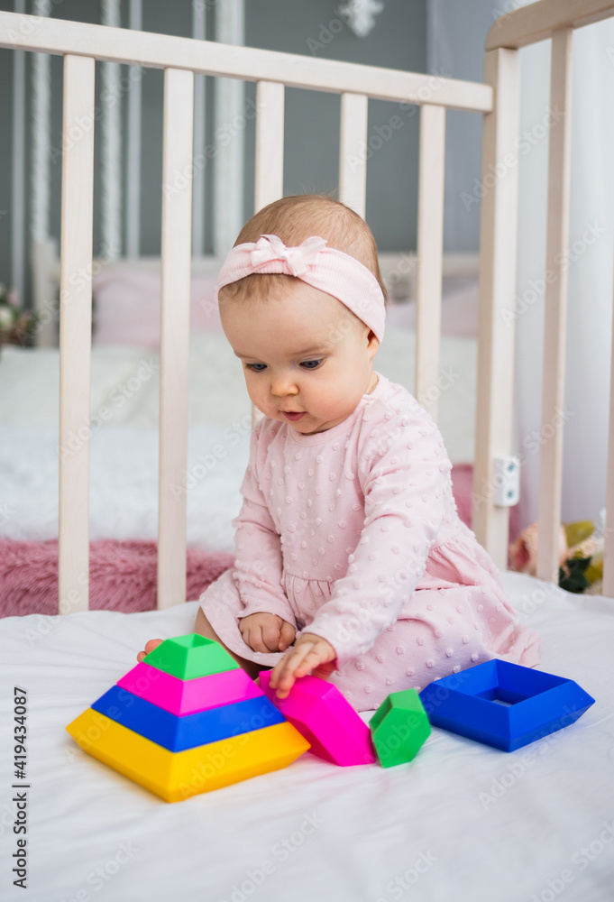 smart baby girl collects a pyramid in the crib in the room. Early child development smart baby girl collects a pyramid in the crib in the room. Early child development