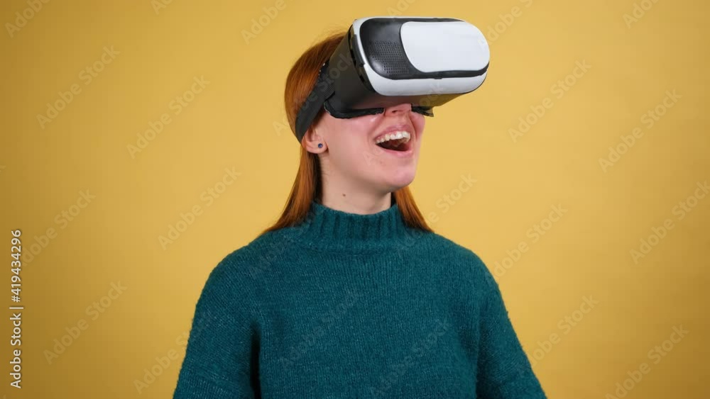 Amazed woman using VR app headset helmet to play simulation game, drawing. Watching virtual reality 3d 360 video. Isolated on yellow background in studio. Girl in VR goggles looking around Amazed woman using VR app headset helmet to play simulation game, drawing. Watching virtual reality 3d 360 video. Isolated on yellow background in studio. Girl in VR goggles looking around