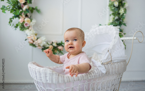 happy baby girl sitting in a retro stroller on a white background with flowers