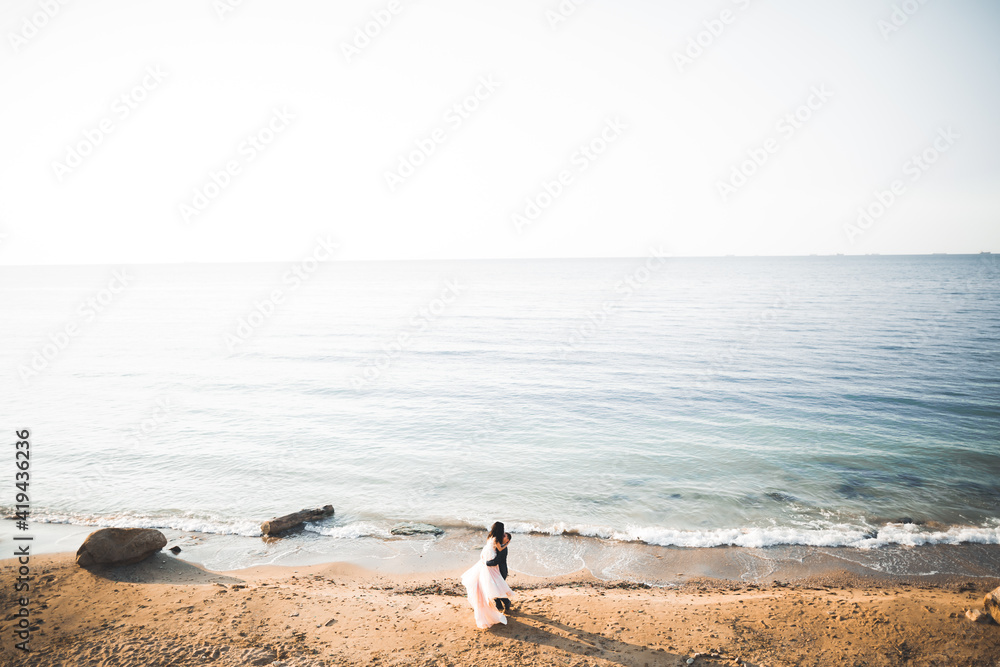 Wedding couple, groom, bride with bouquet posing near sea and blue sky Wedding couple, groom, bride with bouquet posing near sea and blue sky