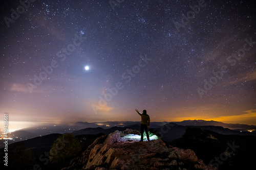 Rear view of a man standing on a mountain at night pointing to sky, Mare De Deu Del Mont, La Garrotxa, Girona, Catalonia, Spain photo