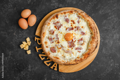 Homemade carbonara pizza with cream sauce, bacon, mozzarella parmesan and egg on a dark background. Top view, side view