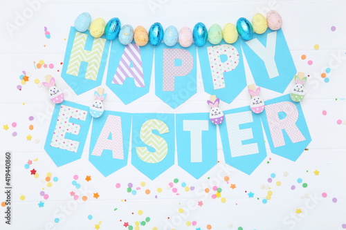 Text Happy Easter with colorful eggs and sprinkles on wooden table