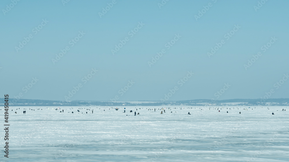 Obraz premium A lot of fishermen for winter fishing on the frozen lake on blue sky background. Leisure activity concept. Space for text.