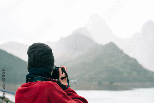Wallpaper Mural Back view anonymous traveler in outerwear standing on massive rock and taking photo while admiring misty mountain ridge surrounding calm lake on autumn day Torontodigital.ca