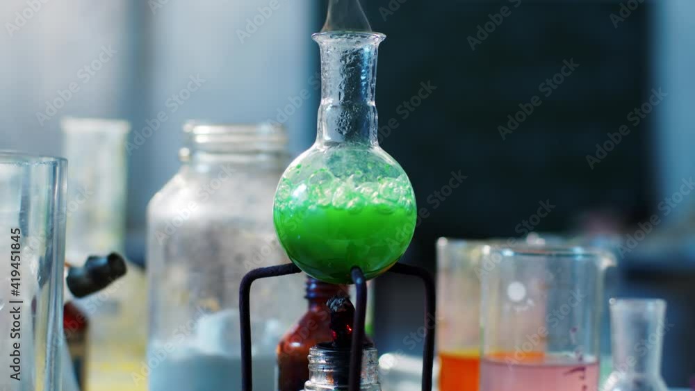 Green chemical solutions boiling in the glass flask in front of the camera in the chemistry laboratory taking video closeup details Green chemical solutions boiling in the glass flask in front of the camera in the chemistry laboratory taking video closeup details