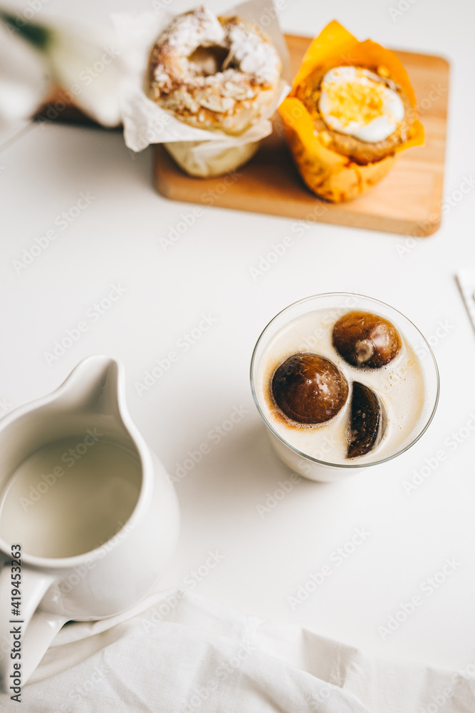 Top view composition of sweet chocolate bombs melting in glass of fresh hot milk placed on table near yummy cupcakes and milk jug Top view composition of sweet chocolate bombs melting in glass of fresh hot milk placed on table near yummy cupcakes and milk jug