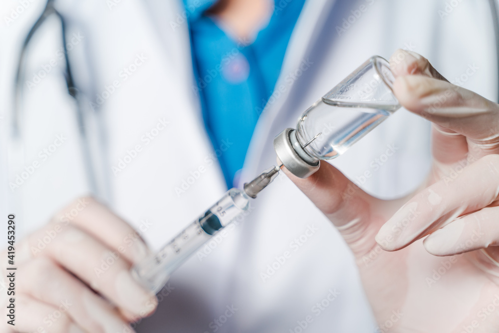 The doctor holding a syringe with Covid-19 vaccines in glass bottle. Covid-19 corona virus treatment concept. The doctor holding a syringe with Covid-19 vaccines in glass bottle. Covid-19 corona virus treatment concept.
