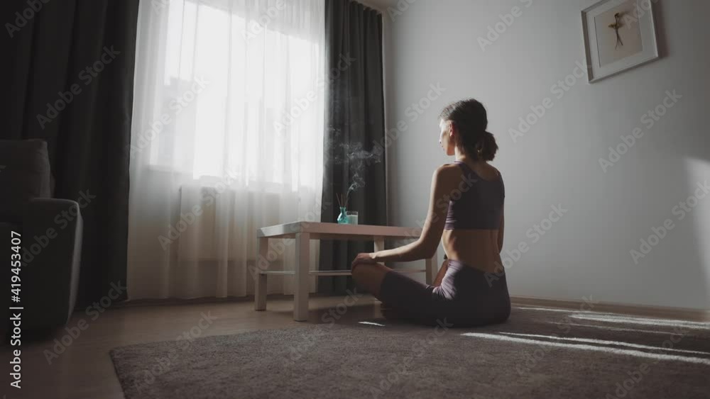 Sporty young woman in activewear sitting on floor and meditating. Pretty female with brown hair burning aromatic sticks for relaxation. Spirituality concept. Sporty young woman in activewear sitting on floor and meditating. Pretty female with brown hair burning aromatic sticks for relaxation. Spirituality concept.