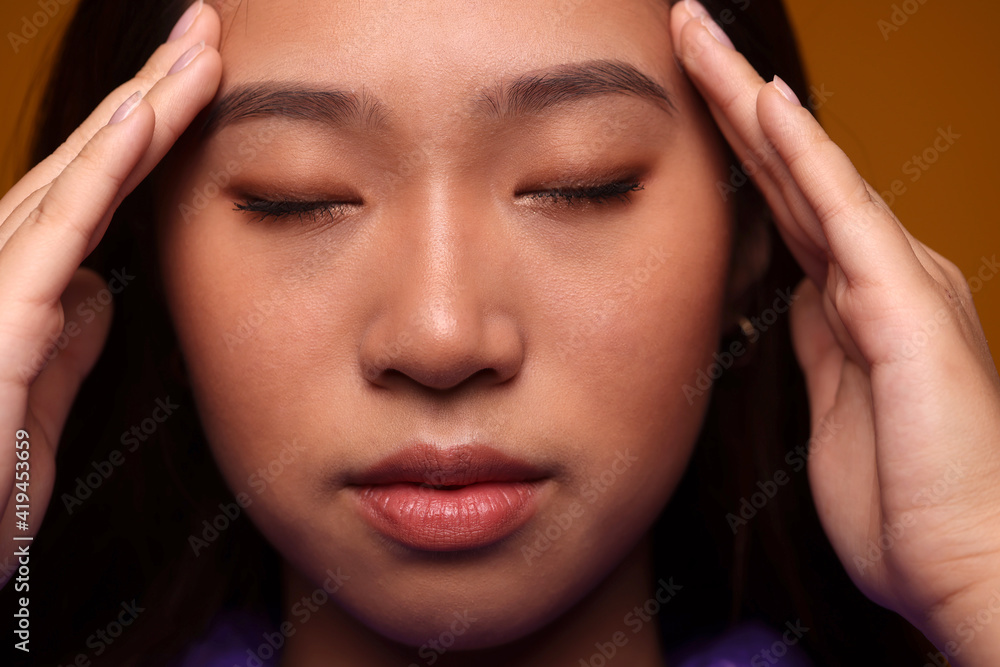 Worried chinese young woman with eyes closed over yellow background Worried chinese young woman with eyes closed over yellow background