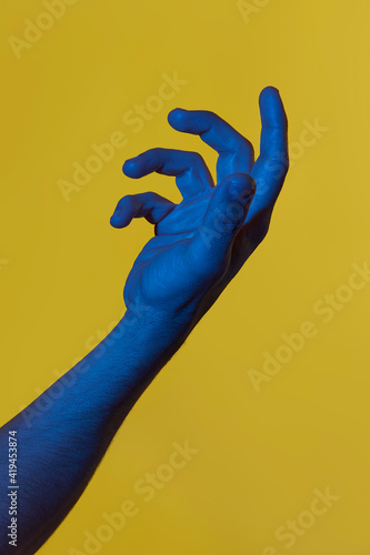 Man's blue hand holding something invisible over yellow background. Isolated vertical photo