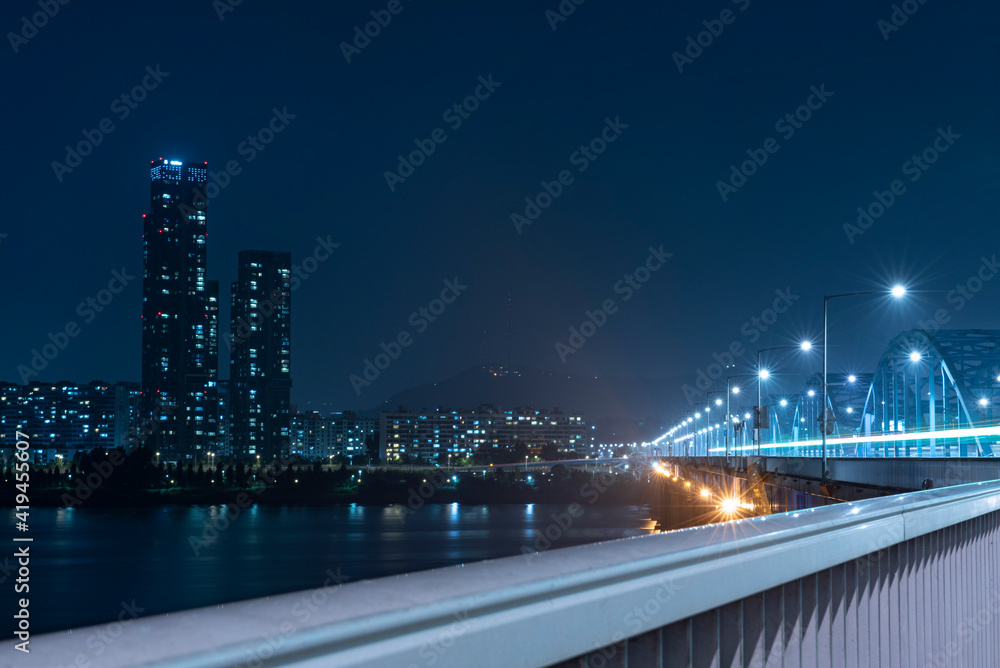 This is a night view of the city from the bridge. The bright shining light and the blue river add a refreshing feeling.