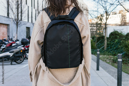 Back view unrecognizable female in warm coat carrying black backpack strolling on urban city street