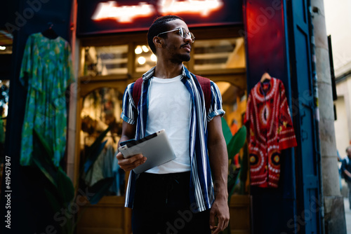 Pensive young ethnic man with tablet standing on street © BullRun