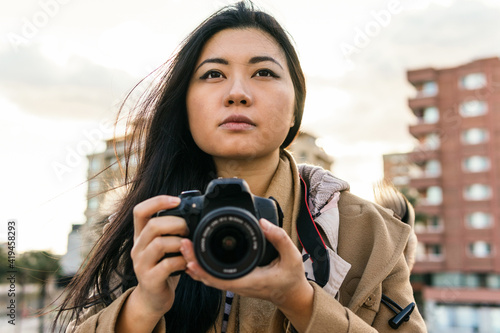 Ethnic Asian female photographer shooting photo on professional photo camera on city street photo