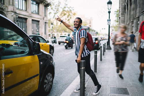 Smiling ethnic man hailing taxi on street