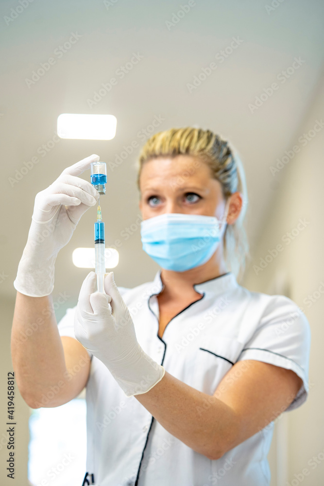 Female doctor in mask and latex gloves filling syringe with liquid medication while working in hospital Female doctor in mask and latex gloves filling syringe with liquid medication while working in hospital